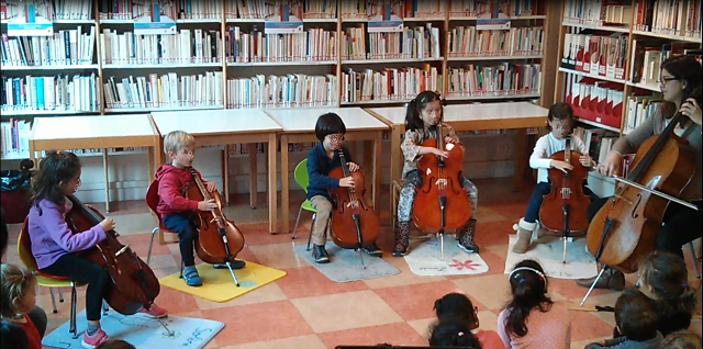 Des enfants jouent du violoncelle devant des classes d'enfants dans une bibliothèque