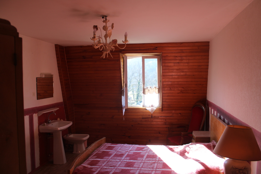 Vue sur la chambre rustique rose : un lit double, une armoire, un lavabo, un bidet, une fenêtre lumineuse donnant sur le Viaur